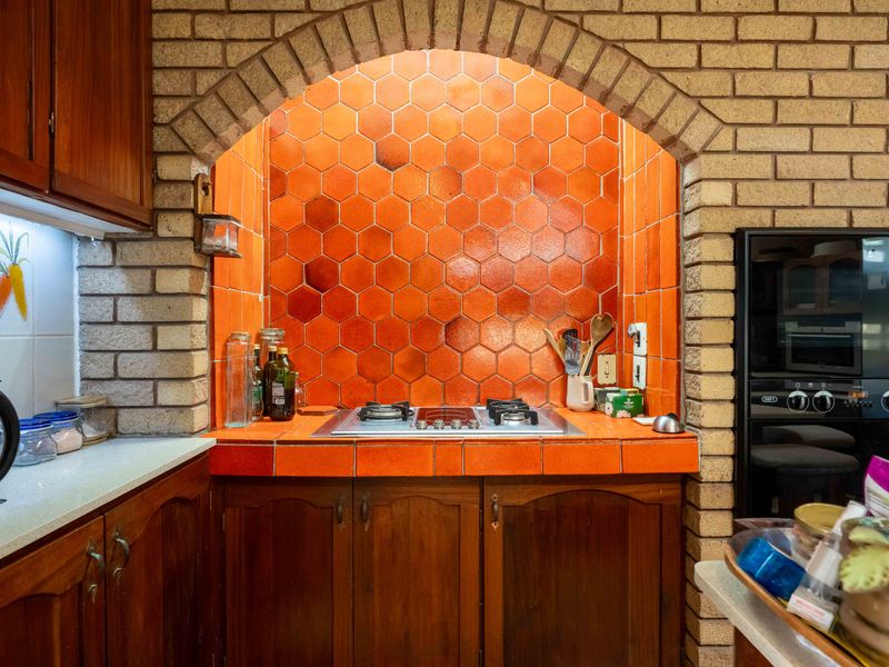 A kitchen featuring a distinctive brick archway over the cooktop, complemented by vibrant orange hexagonal tile backsplash and traditional wooden cabinetry.