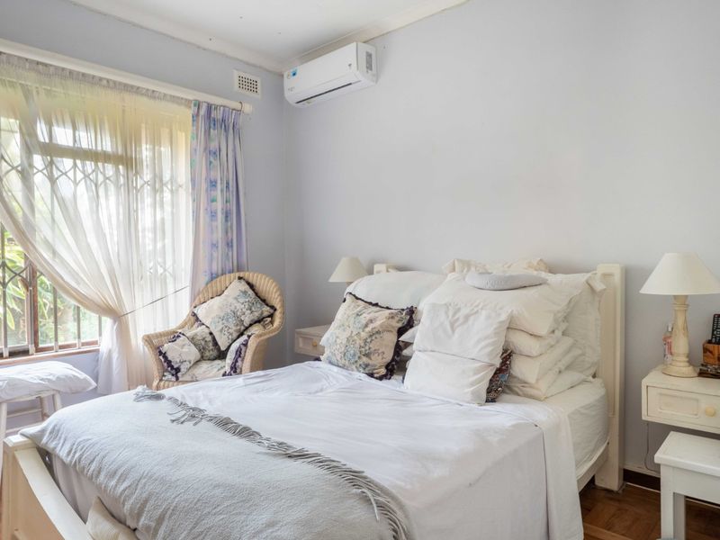 A bedroom featuring parquet flooring, a wall-mounted split-system air conditioner, and a window fitted with a security gate.