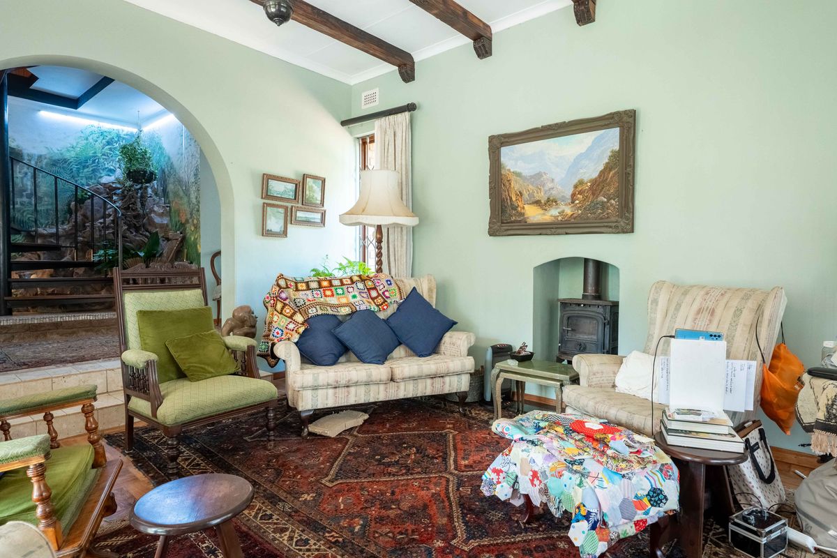 A cozy living room featuring exposed timber ceiling beams, a cast iron fireplace, and an arched entryway leading to an adjacent space.