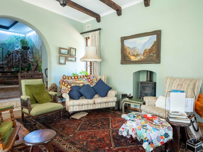 A cozy living room featuring exposed timber ceiling beams, a cast iron fireplace, and an arched entryway leading to an adjacent space.