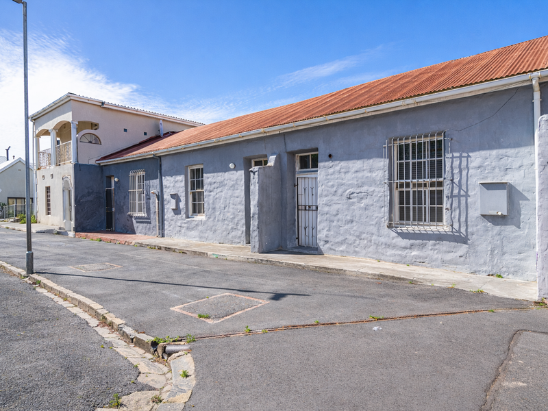 Street-facing facade of a single-story masonry house featuring a corrugated iron roof and security bars on windows.