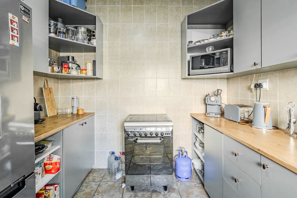 A compact kitchen featuring grey cabinetry, wooden countertops, tiled backsplash, and a freestanding oven, providing a functional workspace.