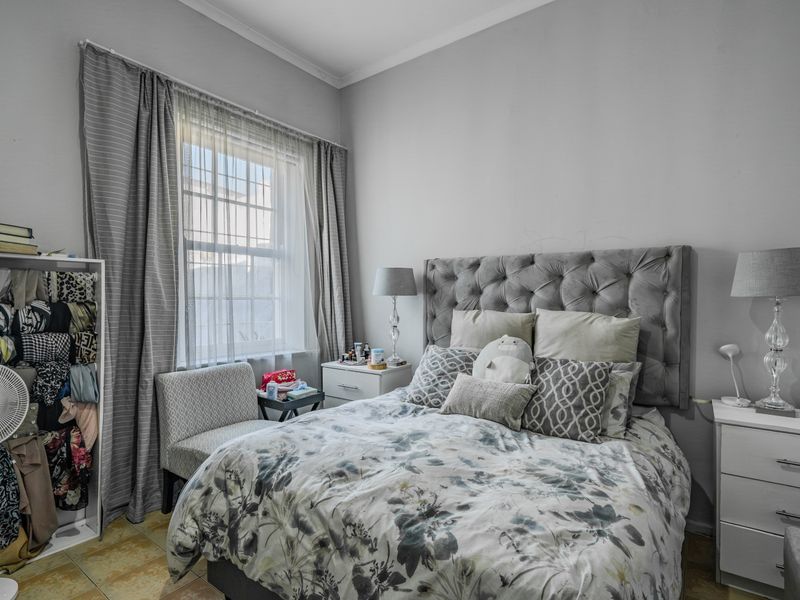 A well-lit bedroom featuring tiled flooring and a window with security bars, providing a functional and comfortable sleeping space.