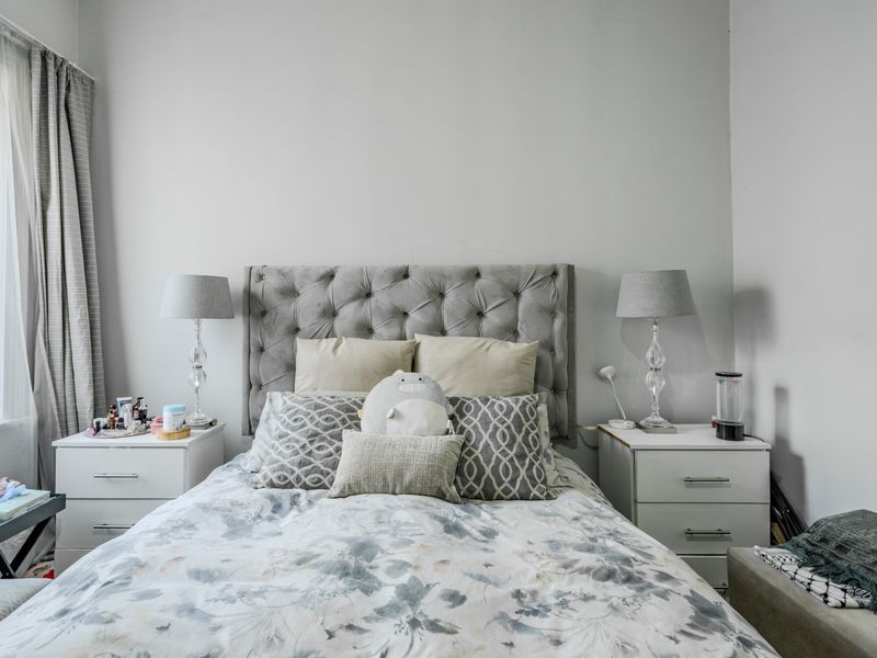 A neutrally decorated bedroom featuring a central bed placement with window access and curtain fixtures.