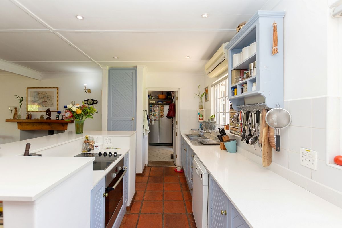 A functional kitchen featuring light blue cabinetry, white countertops, tiled flooring, and a built-in oven and hob, with an adjacent scullery area.