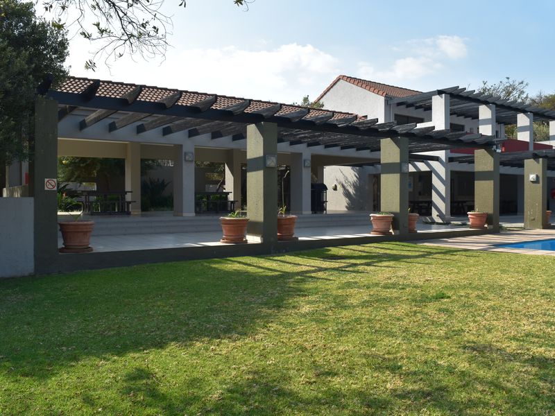 A well-maintained outdoor pool area featuring a large covered pergola, tiled patio space, and a manicured lawn.