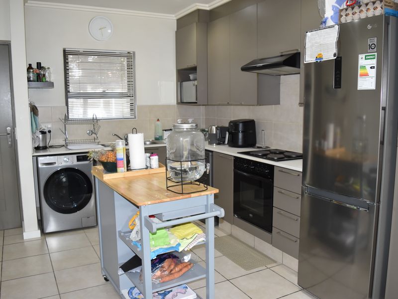 A functional kitchen featuring modern grey cabinetry, tiled backsplash, built-in oven with hob, extractor fan, and tiled flooring.