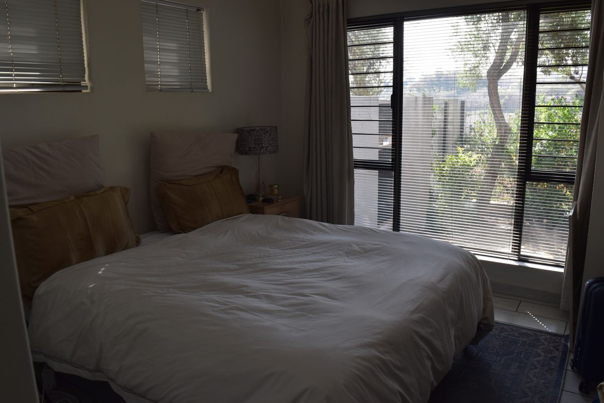 A bedroom featuring large windows with security bars and venetian blinds, offering natural light and a view of the exterior greenery.