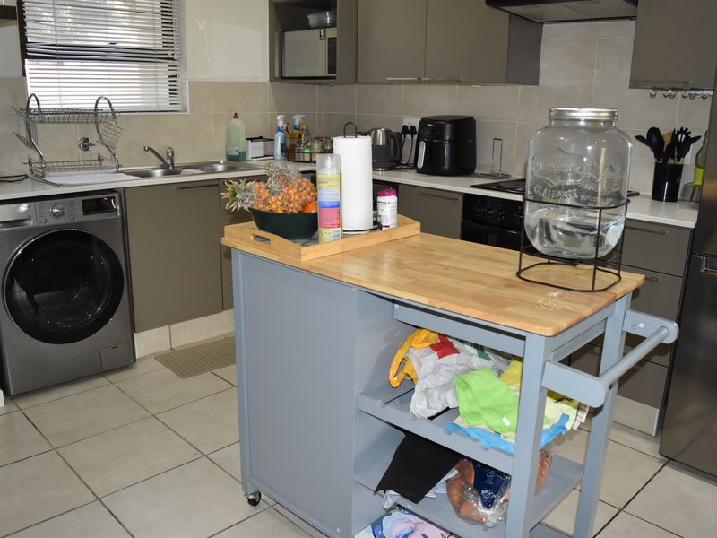 A functional kitchen featuring modern grey cabinetry, tiled backsplash, integrated oven with extractor fan, and tiled flooring with a dedicated space for laundry appliances.
