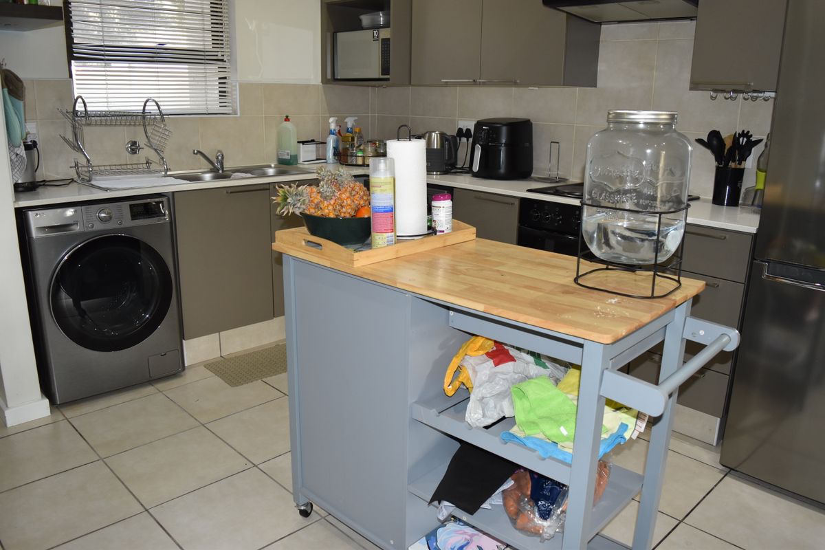 A functional kitchen featuring modern grey cabinetry, tiled backsplash, integrated oven with extractor fan, and tiled flooring with a dedicated space for laundry appliances.