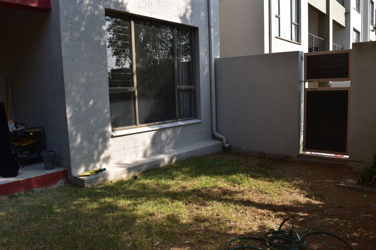 A private rear garden area featuring a small lawn, boundary wall, and access gate, adjacent to the apartment building exterior.
