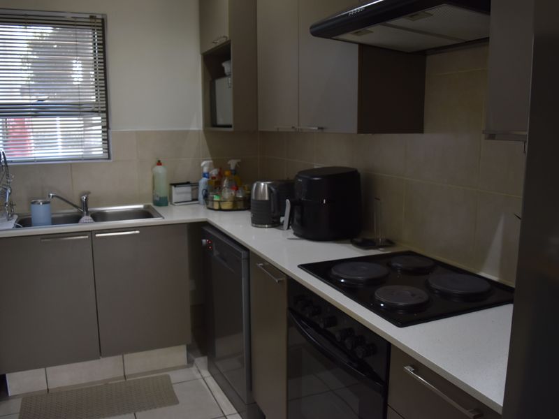 A functional kitchen featuring modern cabinetry, a built-in oven with electric hob, extractor fan, and a stainless steel sink with tiled backsplash.