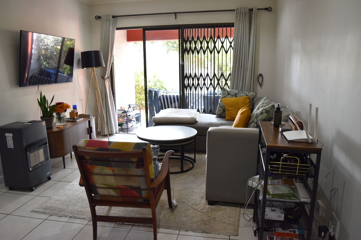 A living room featuring tiled flooring and a sliding glass door with a security gate, providing access to an outdoor area.