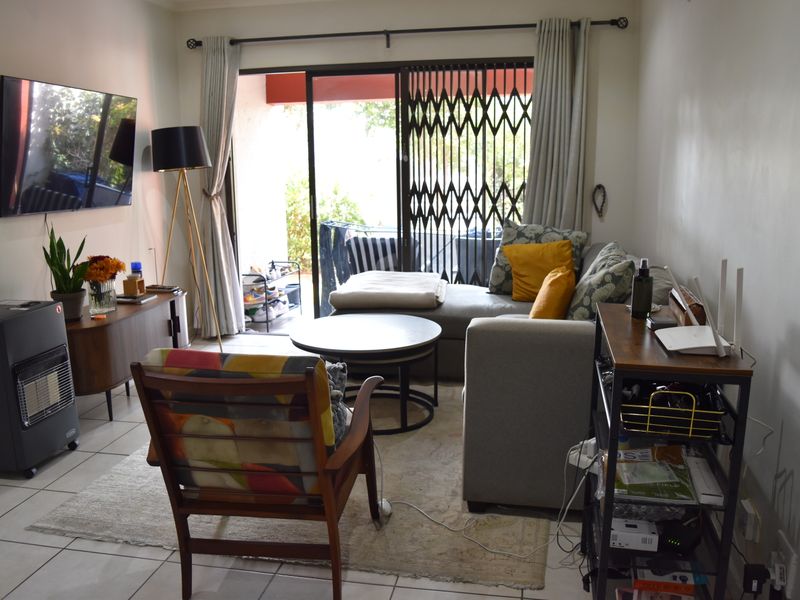 A living room featuring tiled flooring and a sliding glass door with a security gate, providing access to an outdoor area.