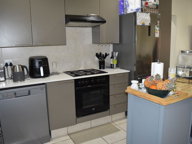 A functional kitchen featuring modern grey cabinetry, a built-in oven with electric hob, extractor fan, and tiled flooring.