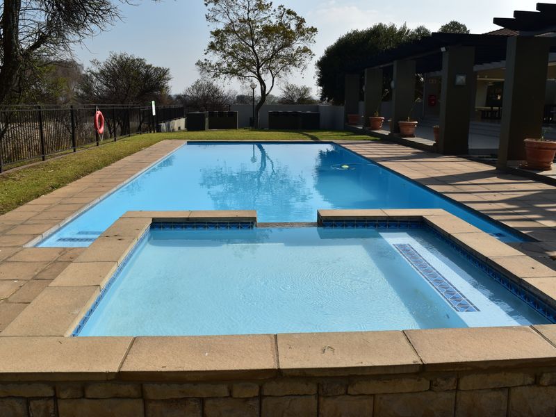 A well-maintained outdoor pool area featuring an integrated spa, paved decking, and a shaded pergola structure.
