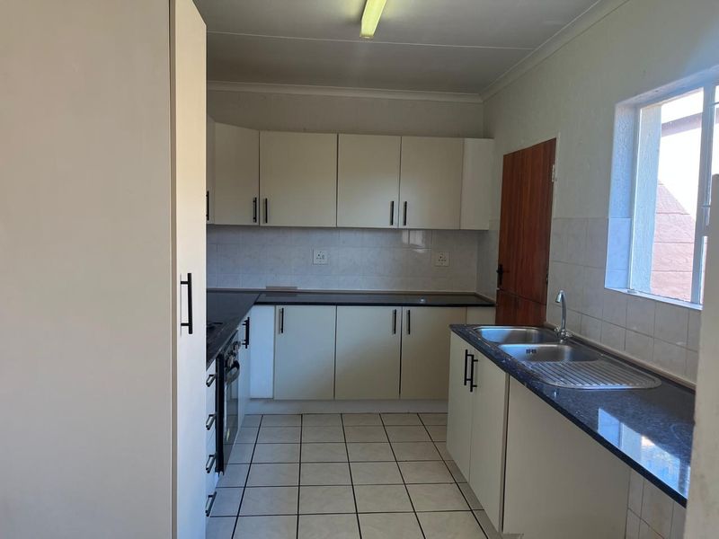 A functional, empty kitchen featuring built-in cabinetry, granite countertops, a double basin sink, and tiled flooring, ready for a modern update.