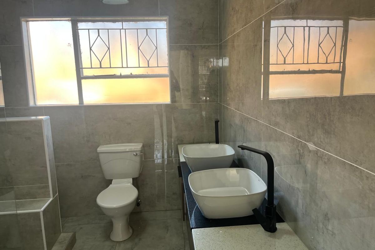 Modern bathroom featuring a double vanity with vessel sinks, black fixtures, and neutral floor-to-ceiling tiling.