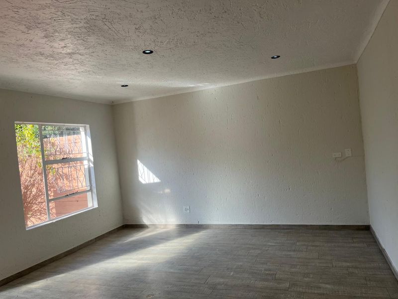 A bright, empty living room featuring modern tiled flooring, recessed downlighting, and a window fitted with security bars.