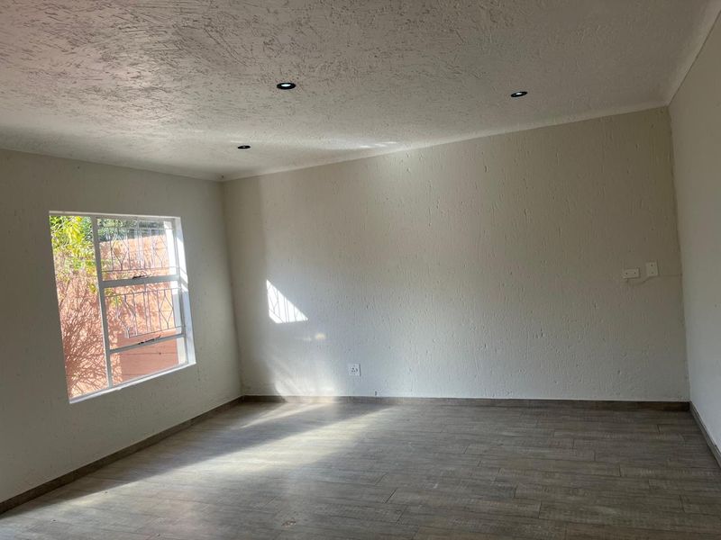 A bright, empty living room featuring modern tiled flooring, textured walls, and recessed downlights, offering a clean and versatile space.