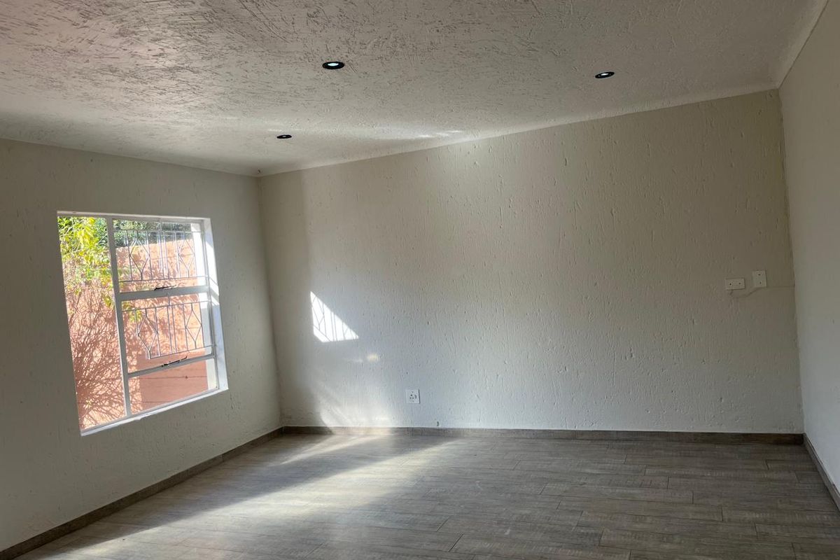 A bright, empty living room featuring modern tiled flooring, textured walls, and recessed downlights, offering a clean and versatile space.