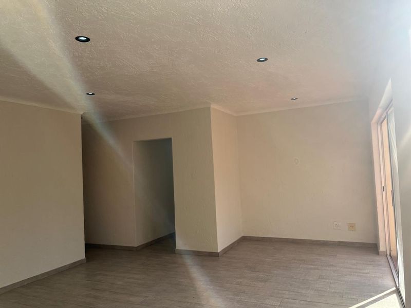 A bright, empty living area featuring modern tiled flooring, recessed downlights, and a sliding glass door providing access to the exterior.