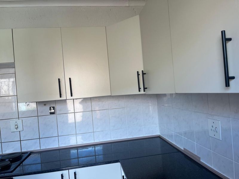 A functional kitchen area featuring white built-in cabinetry, black granite countertops, and a tiled backsplash with an integrated electric hob.
