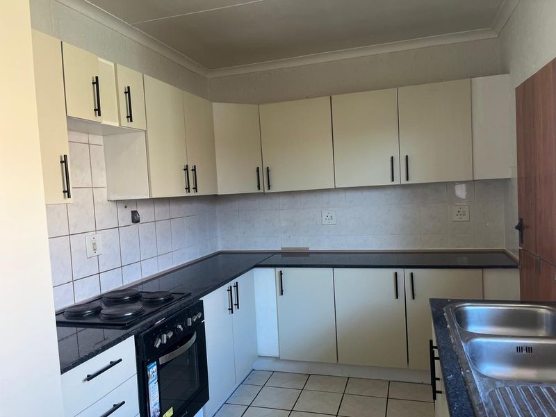 A functional kitchen featuring light-toned cabinetry, dark granite countertops, a built-in oven and hob, and a double stainless steel sink with tiled backsplash.