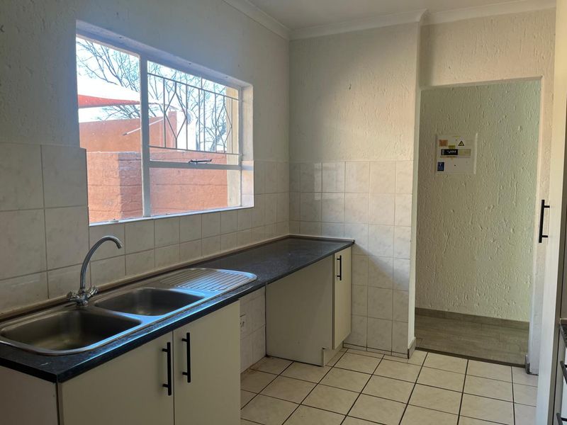 A functional kitchen featuring a double stainless steel sink, laminate countertops, tiled splashbacks, and ample base cabinetry, with an adjacent utility area.