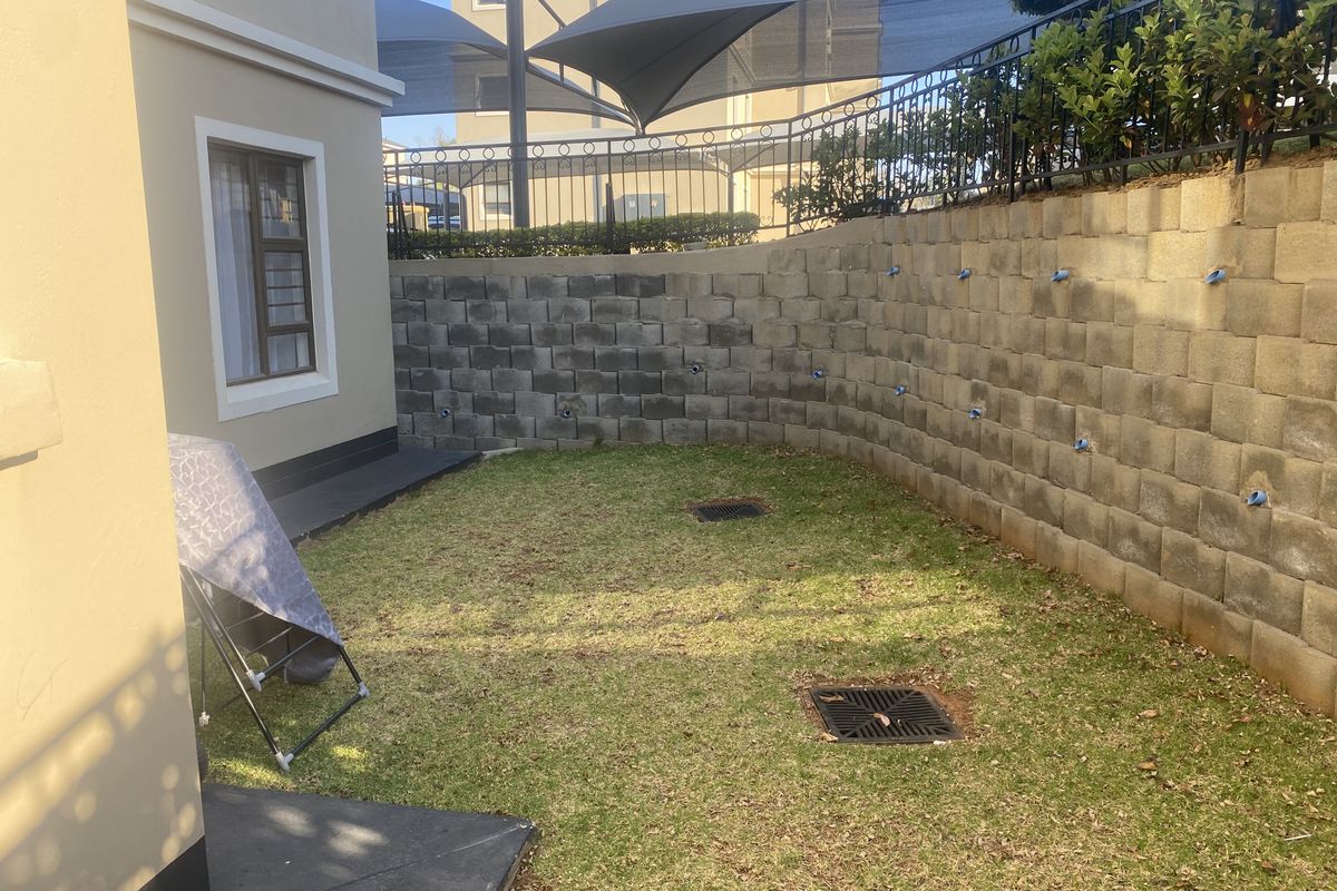 A private rear garden area featuring a structured retaining wall, drainage system, and perimeter fencing with overhead shade sails.