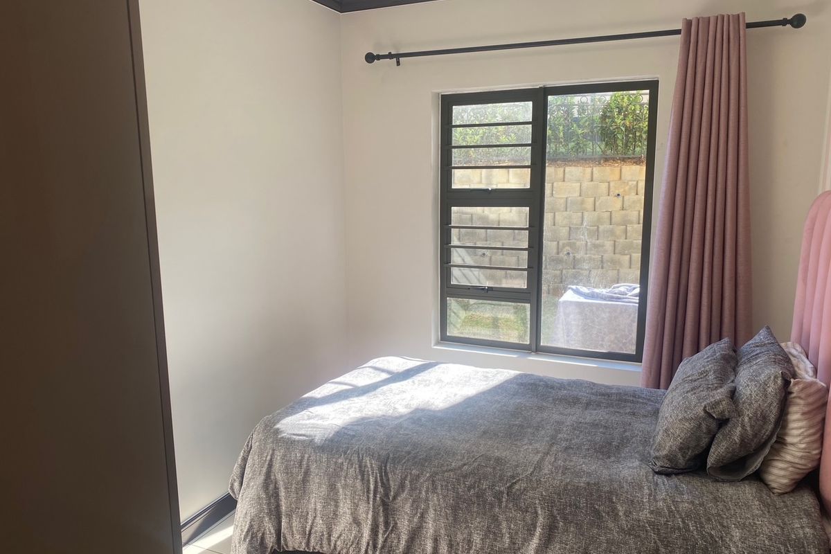 A well-lit bedroom featuring neutral walls, dark crown molding, and an aluminium-framed window overlooking a rear retaining wall.
