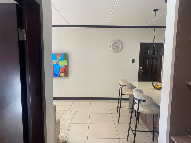An open-plan living and kitchen area featuring tiled flooring, a breakfast bar with pendant lighting, and a solid wood entrance door.