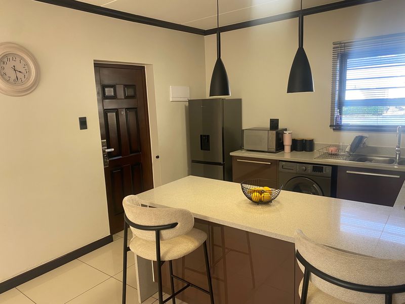 Modern kitchen featuring a central island with stone countertops, sleek cabinetry, integrated appliances, and stylish pendant lighting, creating a functional and contemporary cooking space.