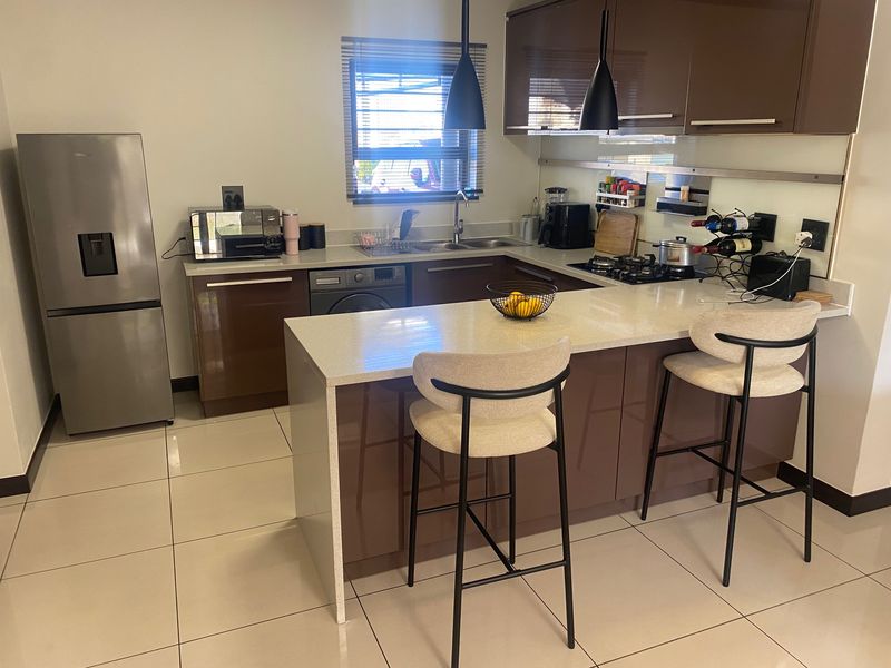 Modern kitchen featuring high-gloss brown cabinetry, stone countertops, a breakfast bar, and integrated gas hob with extractor fan.