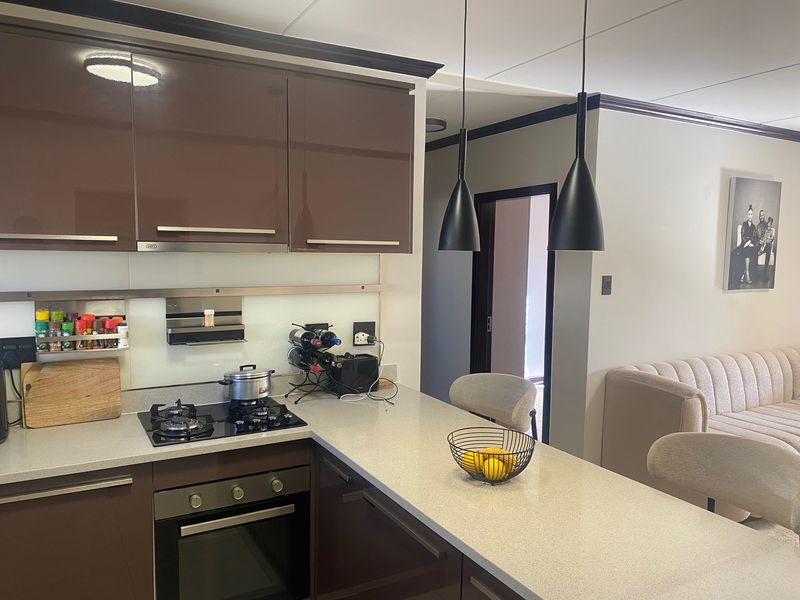 Modern open-plan kitchen featuring high-gloss cabinetry, stone countertops, integrated gas hob, and oven, seamlessly flowing into the adjacent living area.