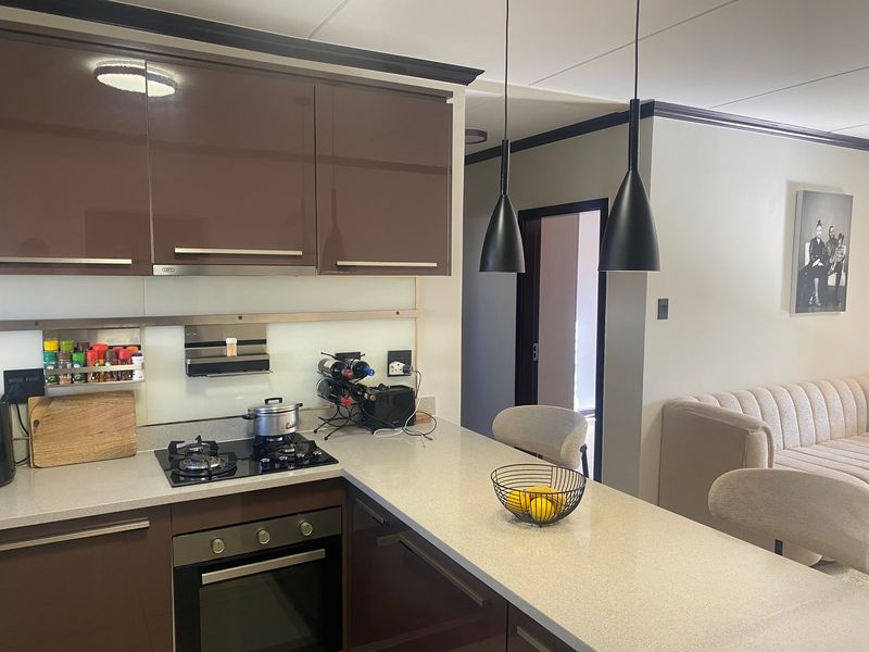 Modern kitchen featuring high-gloss brown cabinetry, stone countertops, integrated gas hob, built-in oven, and stylish pendant lighting.