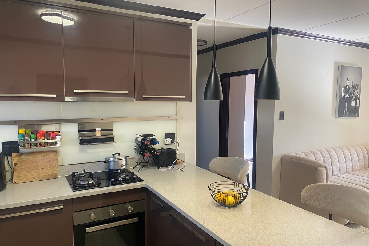 Modern kitchen featuring high-gloss brown cabinetry, stone countertops, integrated gas hob, built-in oven, and stylish pendant lighting.