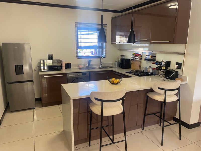Modern kitchen featuring glossy brown cabinetry, stone countertops, a breakfast bar, gas hob, and tiled flooring in an open-plan layout.