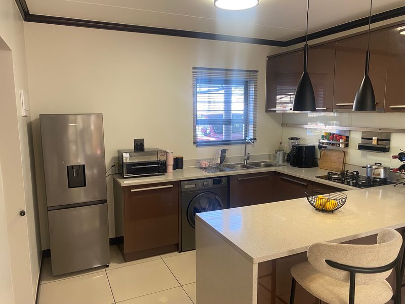 Modern kitchen featuring dark gloss cabinetry, stone countertops, integrated appliances, gas hob, and tiled flooring with a functional breakfast bar layout.