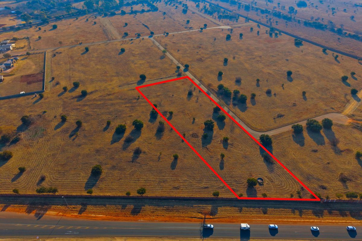 An aerial view of a vacant residential plot with clear boundary markings, situated in a developing estate area.