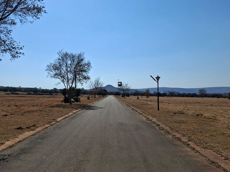 A paved access road leading through an open residential land plot with clear views of the surrounding landscape.
