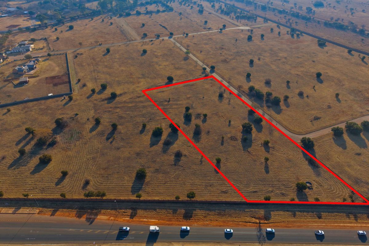 Aerial view of a vacant residential plot with clear boundary markings, situated in a developing estate with road access.