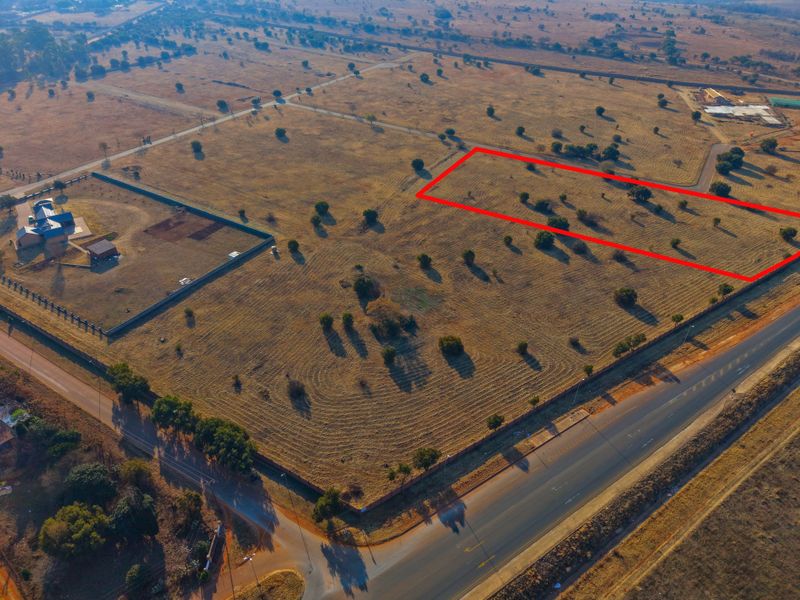 An aerial view of a vacant residential plot highlighted in red, situated in a developing area with established road access and boundary fencing.