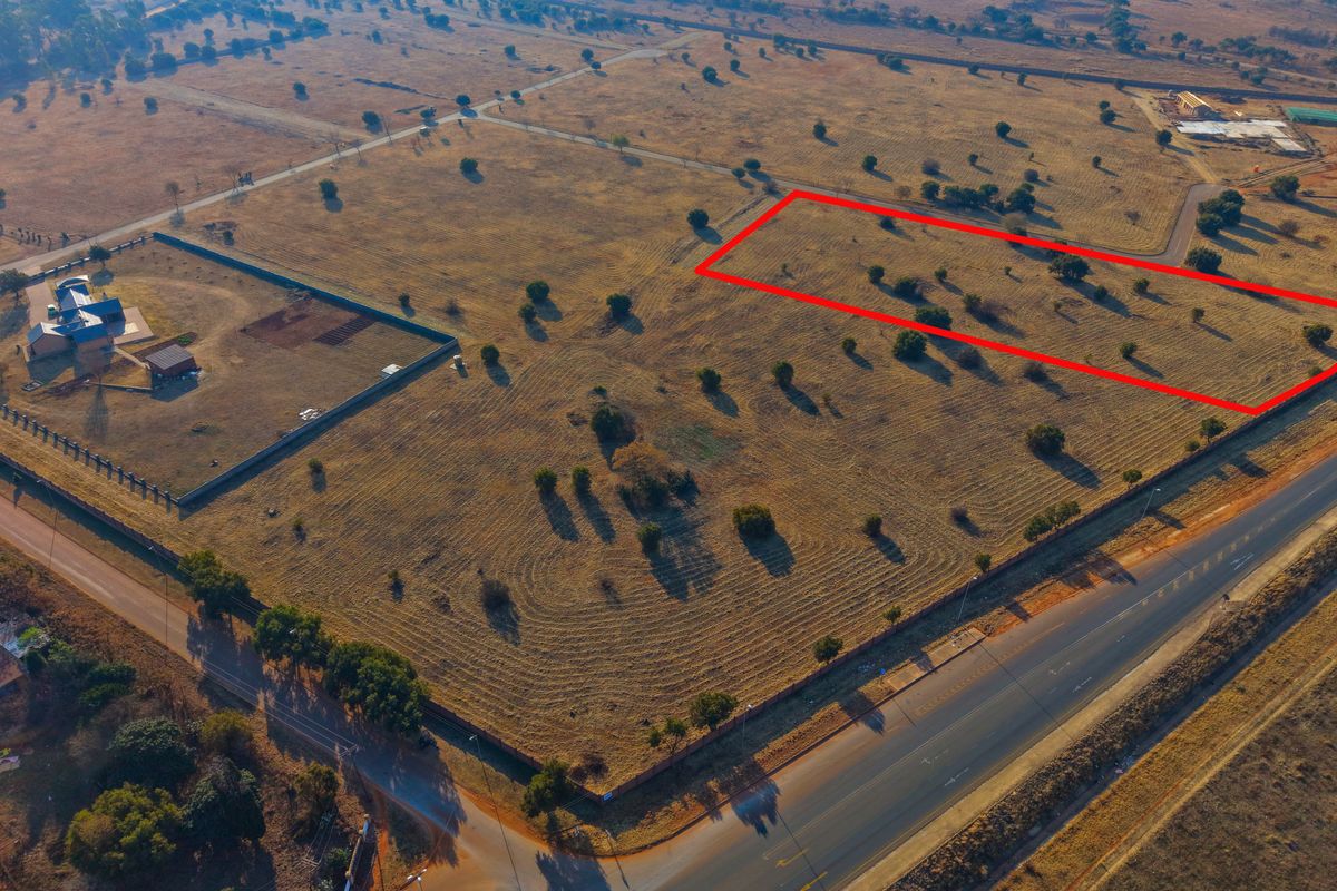 An aerial view of a vacant residential plot highlighted in red, situated in a developing area with established road access and boundary fencing.