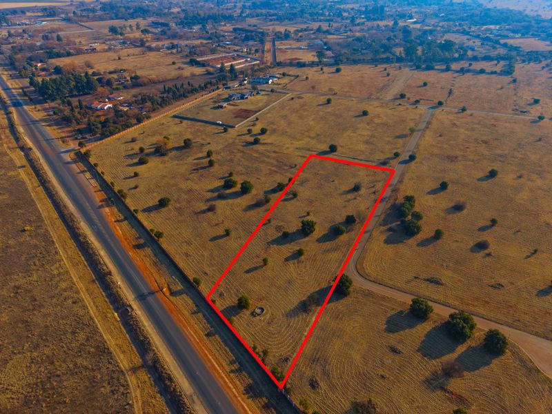 Aerial view of a vacant residential plot with clear boundary markings, situated in a rural estate setting with surrounding road access.