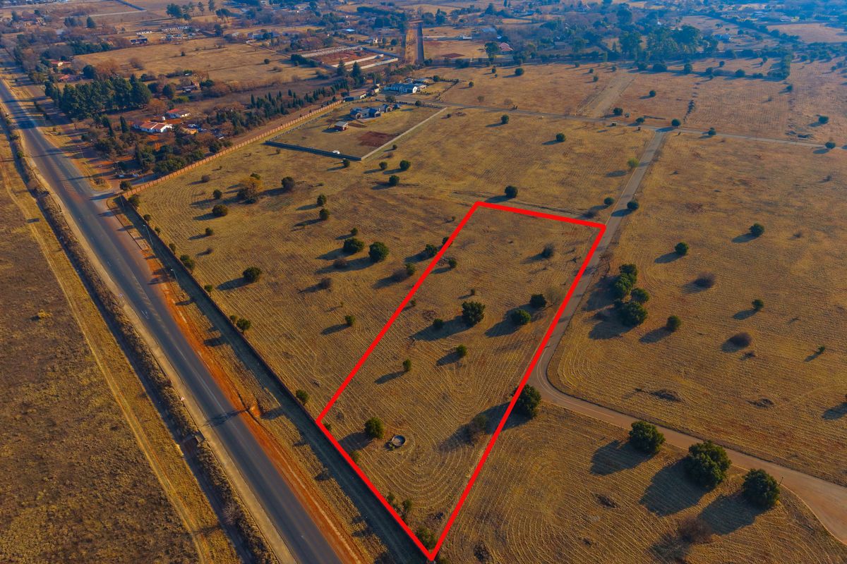 Aerial view of a vacant residential plot with clear boundary markings, situated in a rural estate setting with surrounding road access.