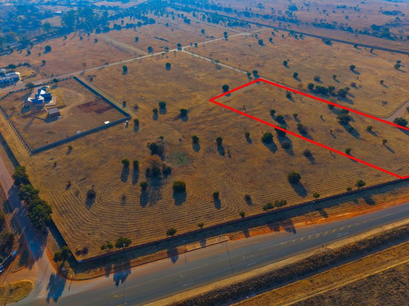 Aerial view of a vacant residential land plot with clear boundary markings, situated near a main road and established residential properties.