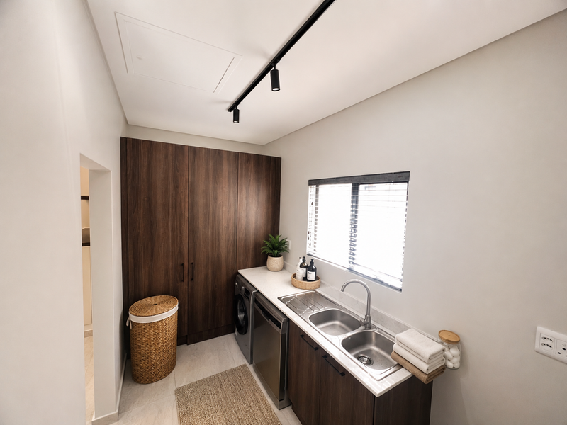 Modern laundry room featuring dark wood cabinetry, a stainless steel double sink, stone-look countertops, and efficient track lighting.