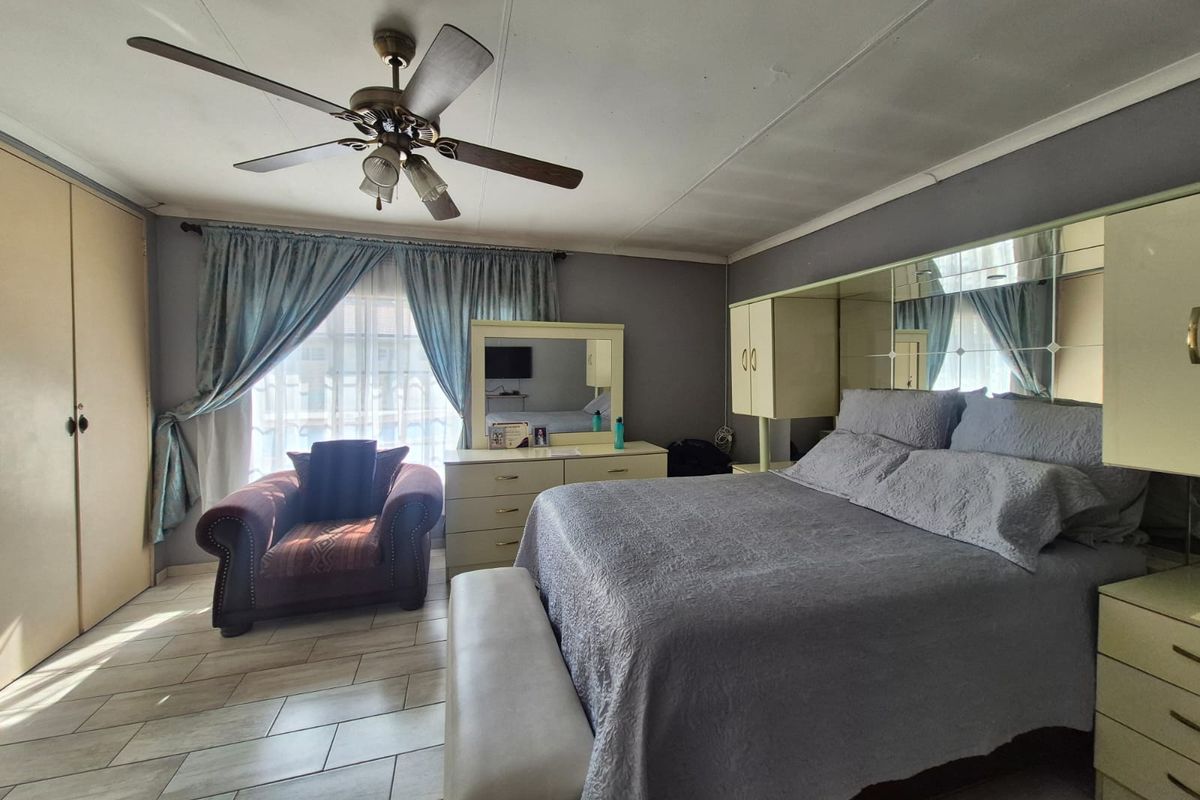 Spacious bedroom featuring built-in cupboards, tiled flooring, and a ceiling fan, offering a functional layout with ample storage space.