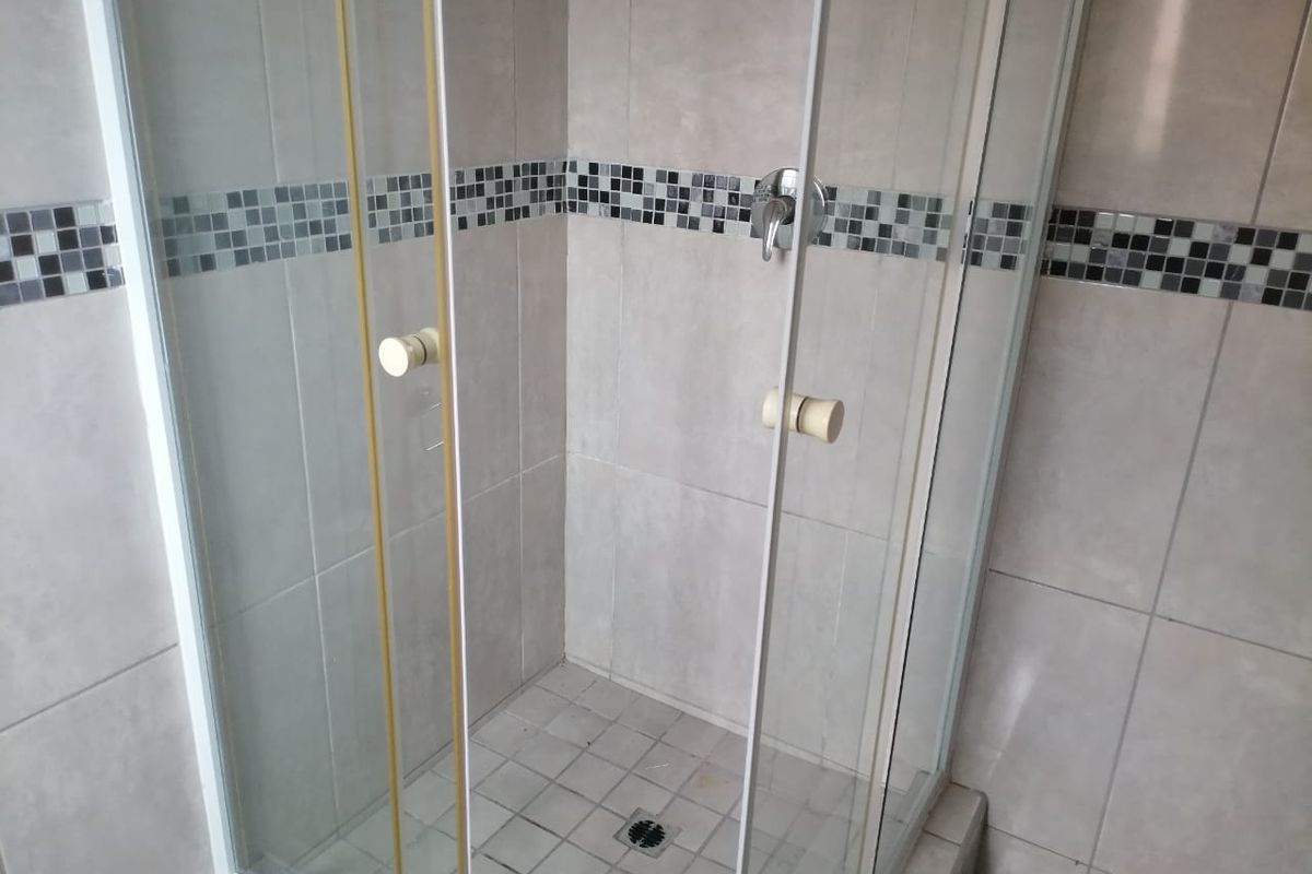 A functional bathroom shower stall featuring a glass enclosure, tiled walls with a decorative mosaic border, and a standard shower mixer.